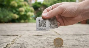 A lightweight aluminium QR code cat tag held next to a small coin for scale.